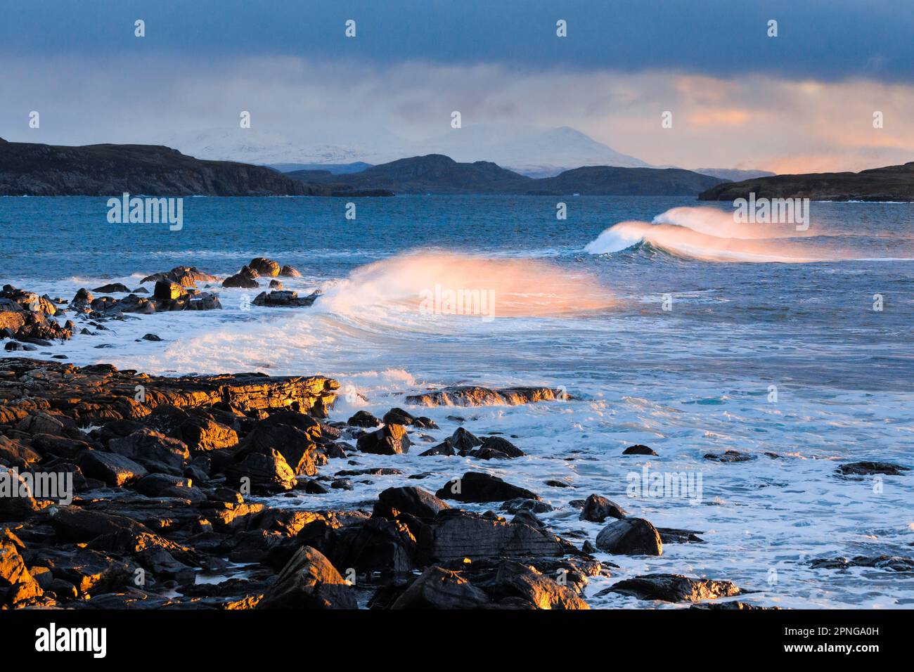 Large waves crash in a winter storm and the swirling spray is illuminated by the warm light of the evening sun, Summer Isles in the background, at Stock Photo