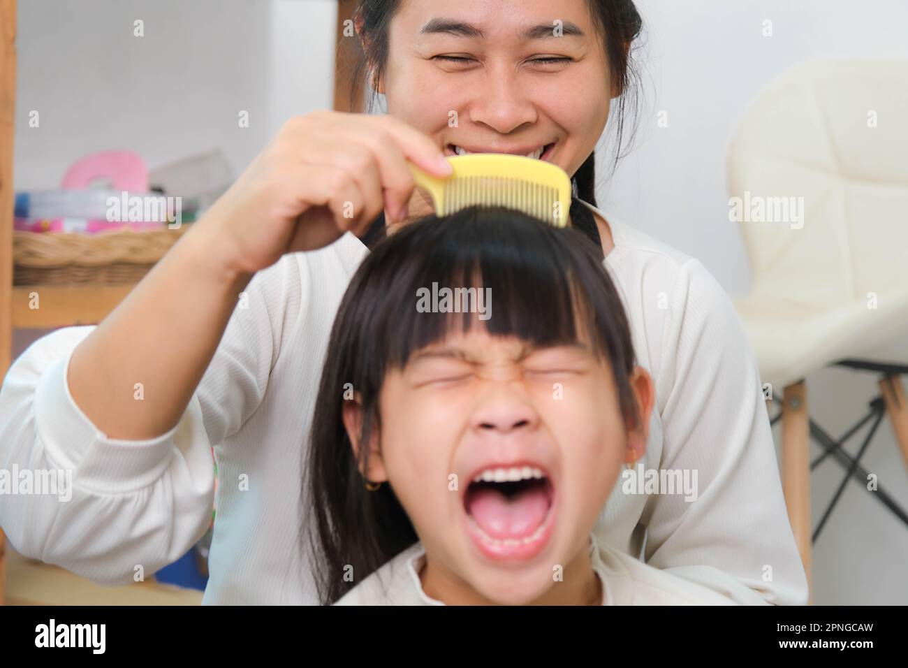 Charming little girl smiling while her beautiful mother combs her daughter's hair. Mother combing her daughter's hair to sit in the room. Happy loving Stock Photo