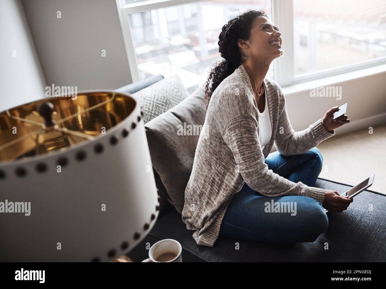 Banking made very simple. a cheerful young woman relaxing on a chair while doing online shopping on a digital tablet at home. Stock Photo