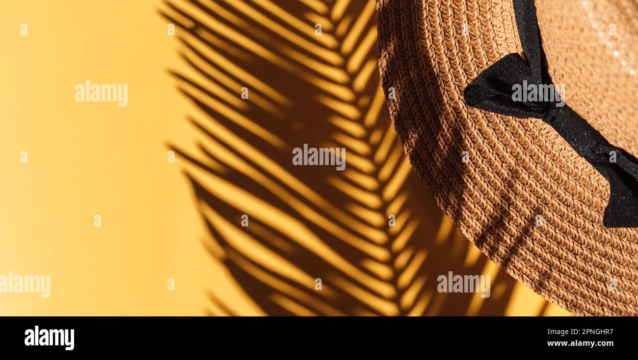 Shadow of palm branch falls on straw hat against yellow background ...