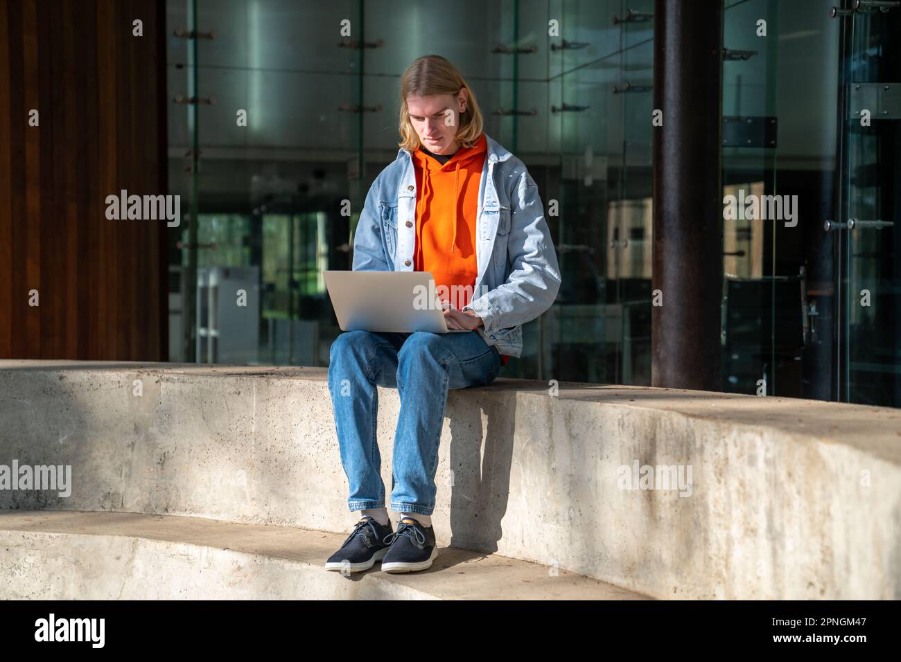 Focused man student studying working on research project sitting on cement steps near university. Stock Photo