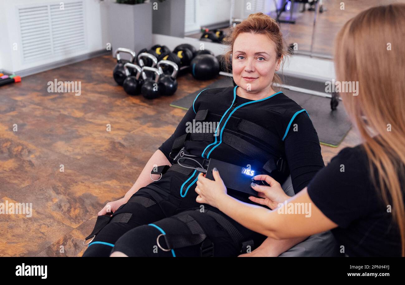 https://c8.alamy.com/comp/2PNH4YJ/blonde-woman-middle-age-sits-on-massage-chair-while-waiting-for-ems-workout-in-modern-gym-young-female-trainer-sets-necessary-parameters-on-electrica-2PNH4YJ.jpg