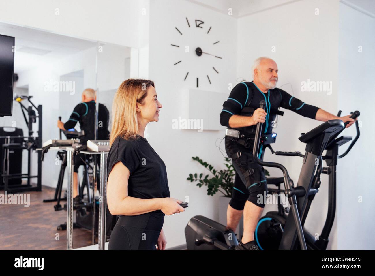 https://c8.alamy.com/comp/2PNH54G/young-smiling-trainer-is-doing-electrical-muscle-stimulation-workout-for-her-client-elderly-greyhaired-man-is-engaged-in-ems-suit-on-elliptical-train-2PNH54G.jpg