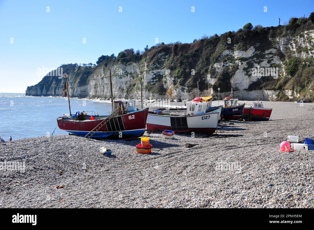 Boats and fishing gear on the shelving pebble beach shelterd by the ...