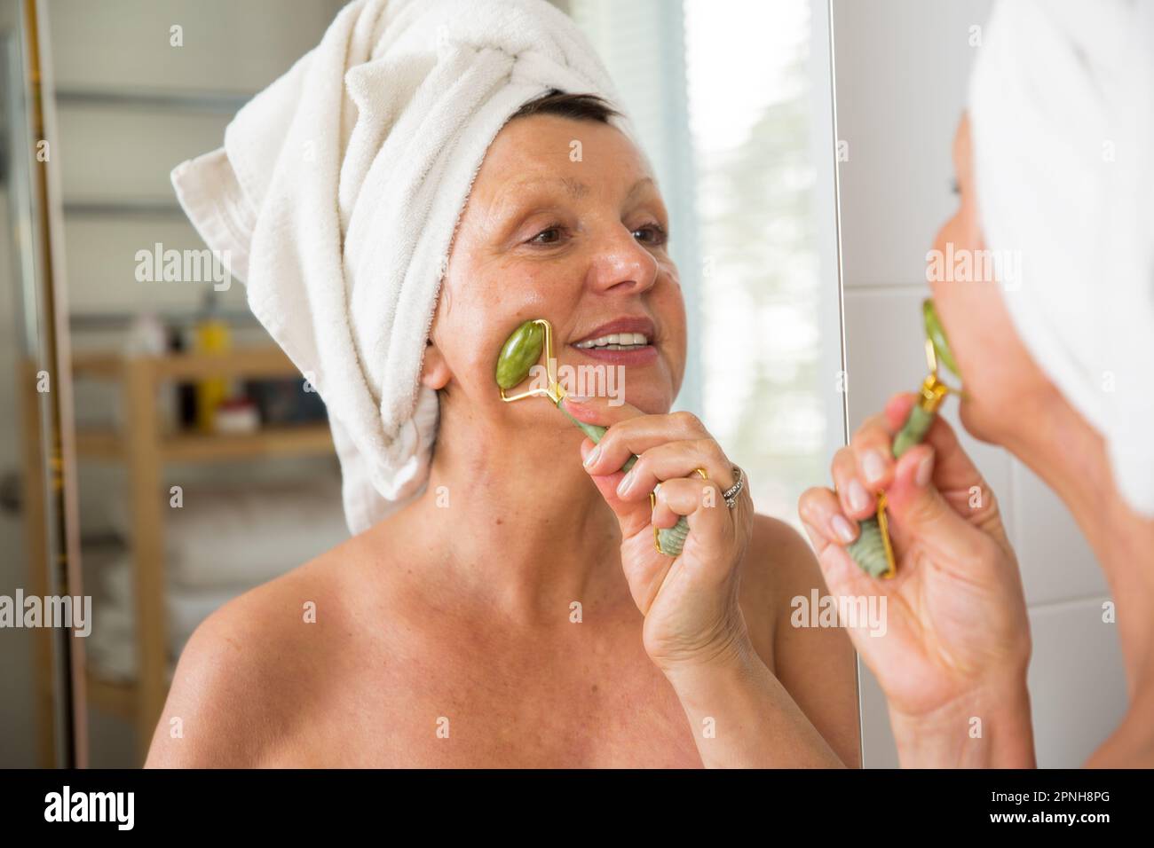 Mature beautiful woman doing facial massage with jade roller. Looking