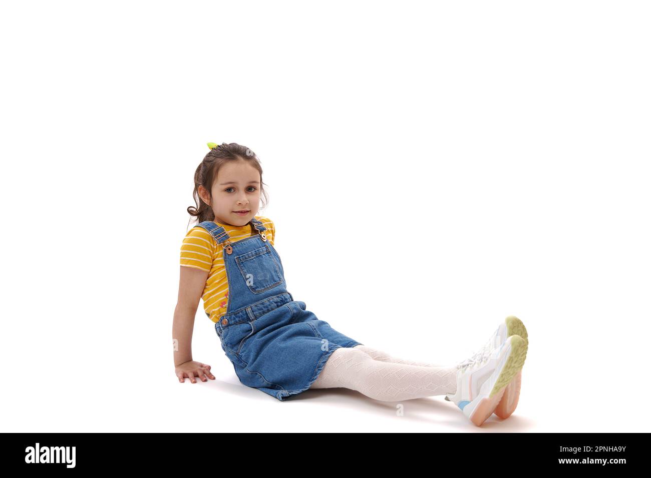 Horizontal full length portrait of Caucasian child girl looking confidently at camera, sitting on white background Stock Photo