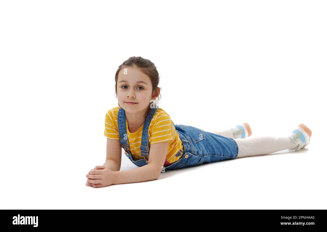 Horizontal full length portrait of Caucasian child girl lying on belly, looking confidently at camera, white background Stock Photo