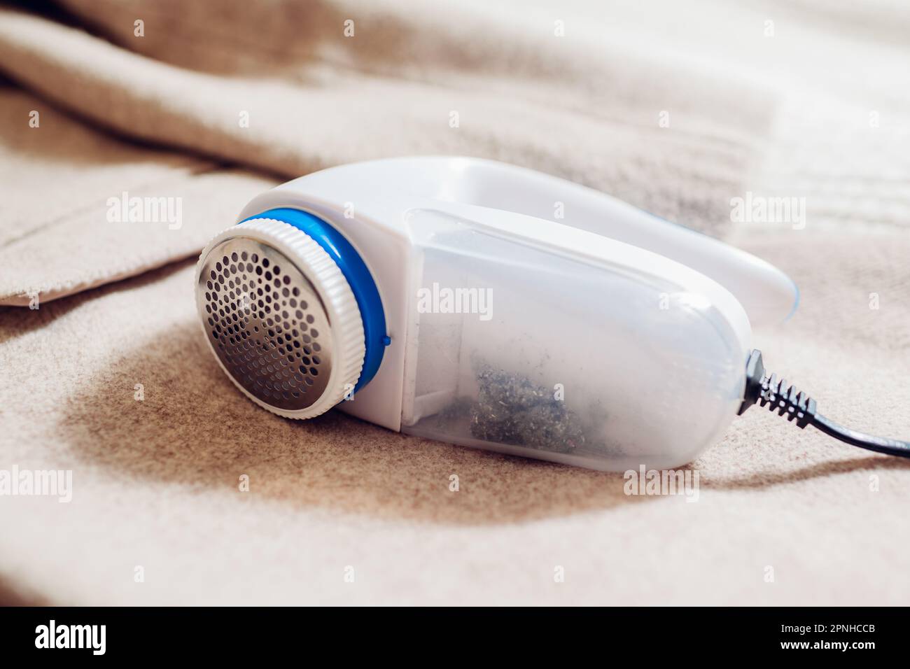 Close up of wired lint remover device. Cleaning clothes with electric fuzz shaver at home. Shaving pilling from coat with modern machine Stock Photo