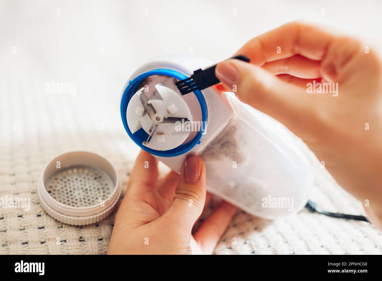 Woman cleaning lint remover razor after shaving fuzz using small brush. Container full of trimmed pilling and dirt. Close up of device Stock Photo