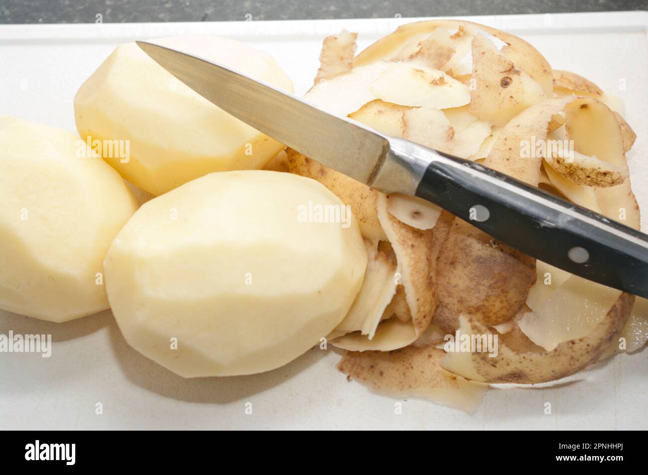 Peeled Maris Piper Potatoes with peel on a white chopping board with a