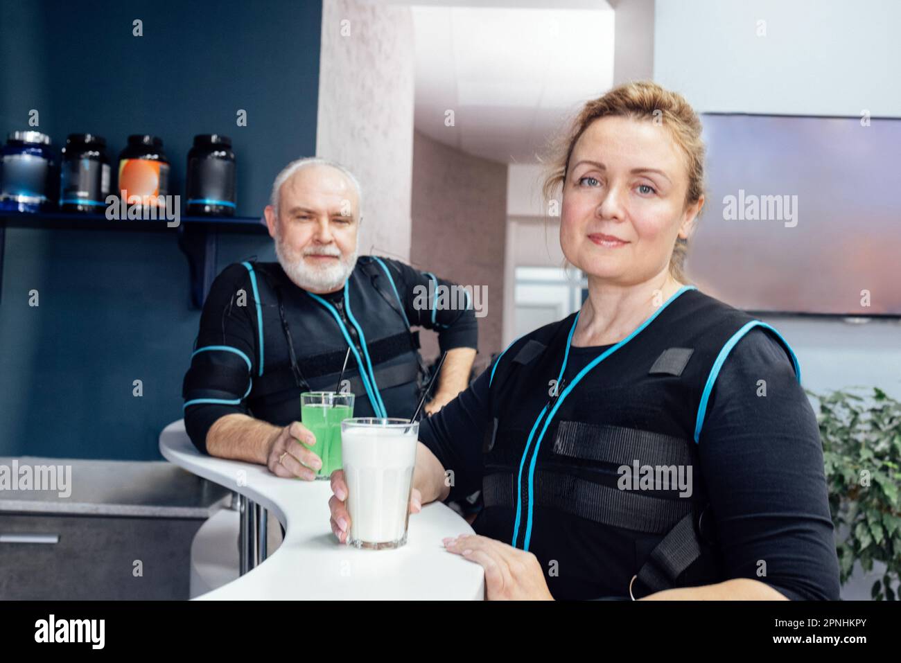 Senior smiling man and woman in ems suits drink shakes in sports bar