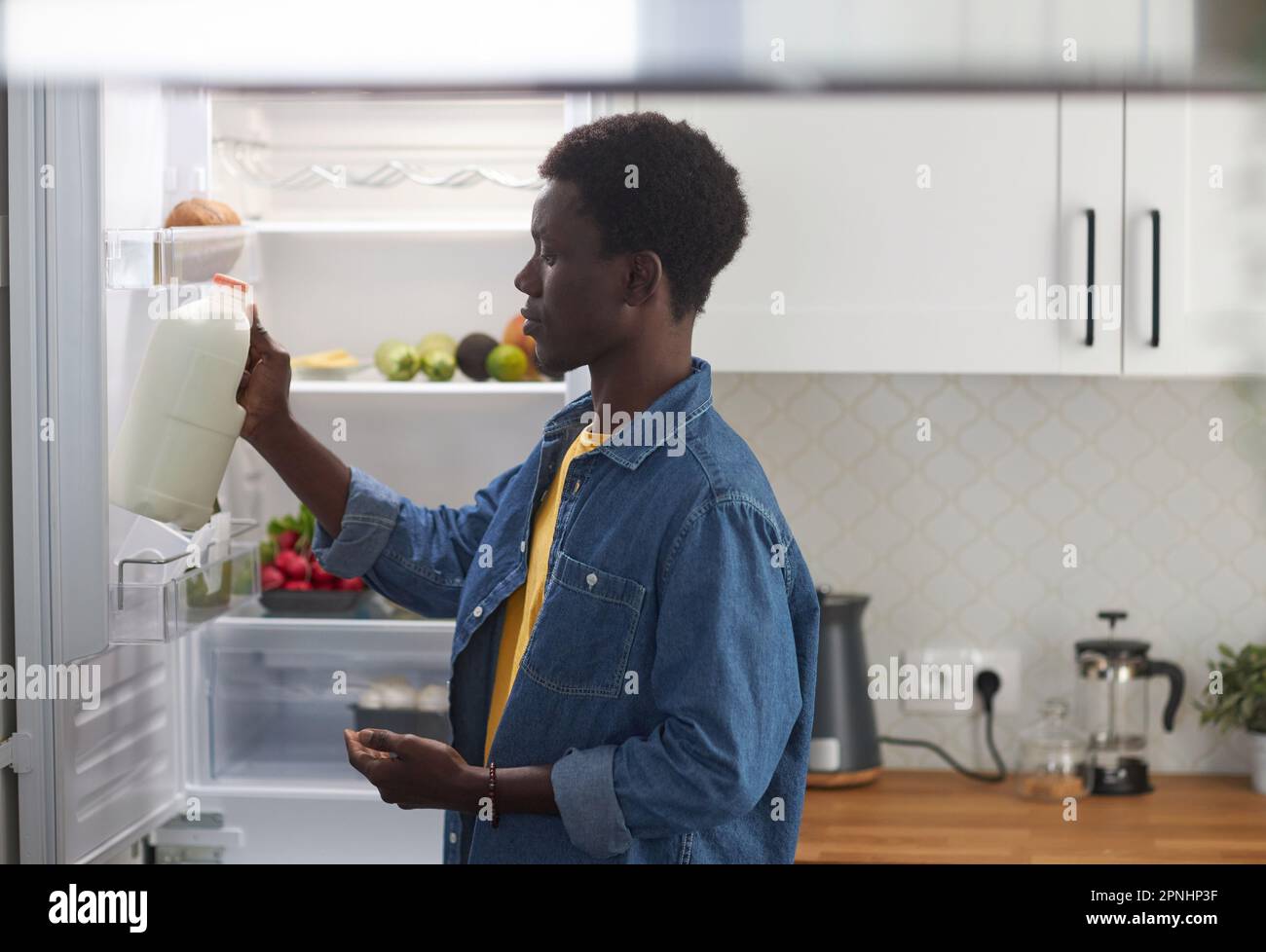 Side view portrait of young black man taking milk from refrigerator while cooking dinner at home Stock Photo