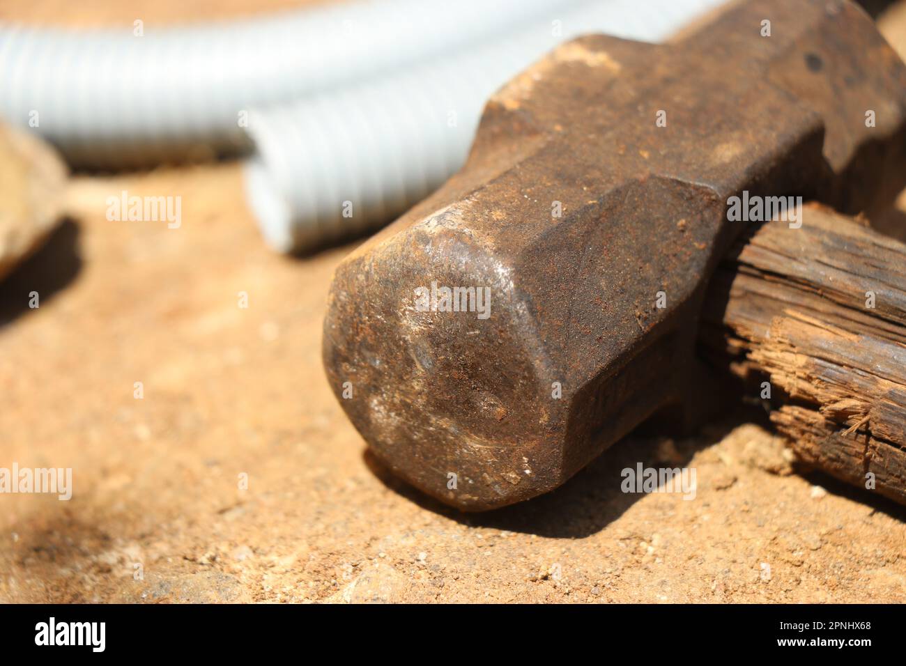 Old and rusty hammer with a broken wooden handle kept on the ground on