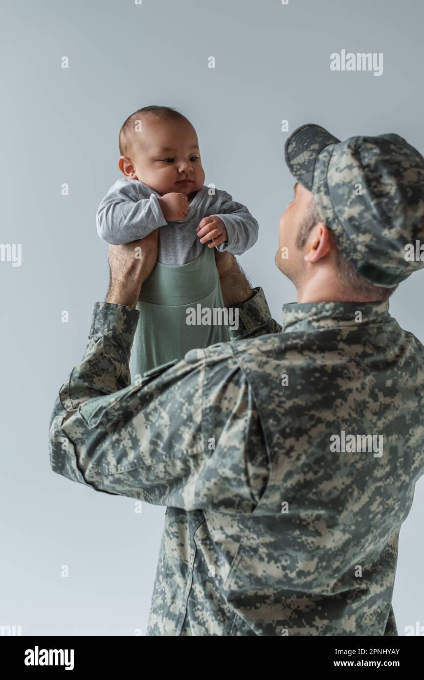 army soldier in military uniform with cap holding infant son in arms isolated on grey Stock
