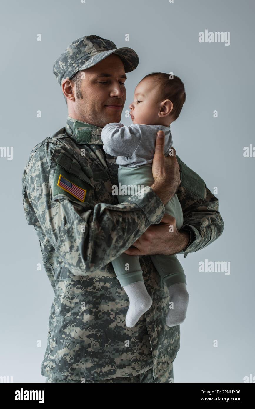 American army soldier in military uniform holding infant son in arms isolated on grey Stock