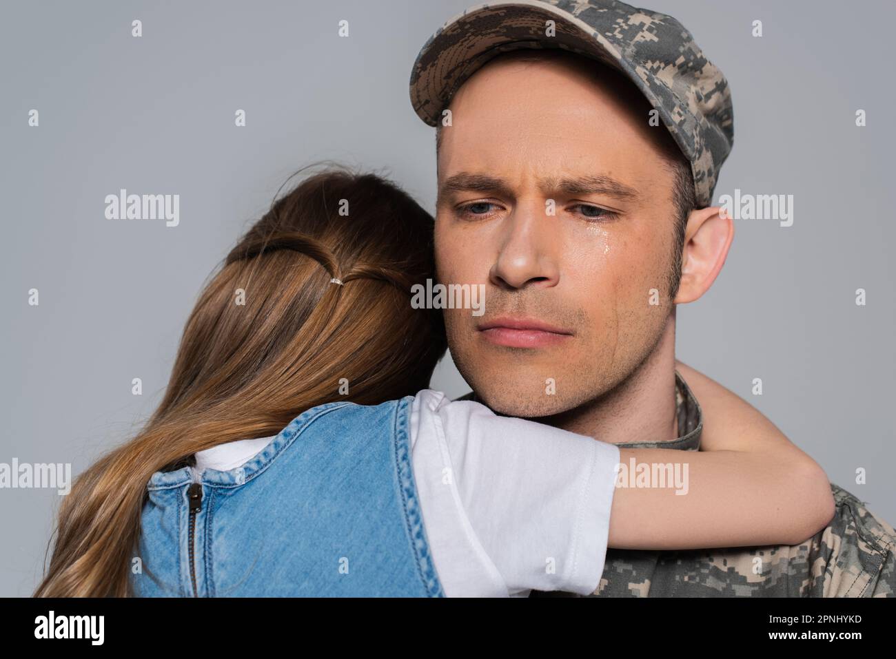 sad serviceman in military uniform crying and hugging with daughter during memorial day isolated on grey Stock Photo