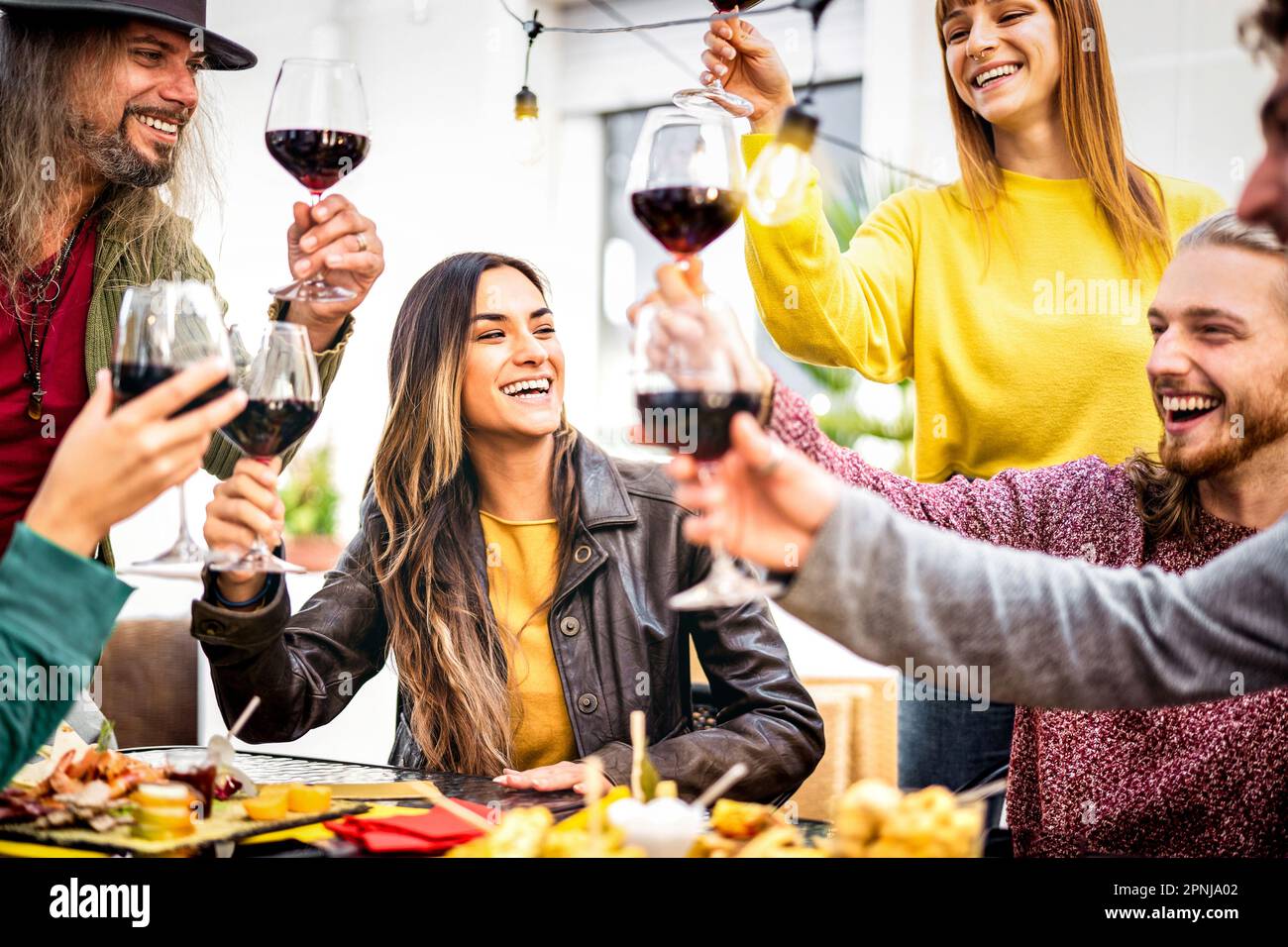 Trendy people having fun toasting red wine out side at home winebar garden - Happy friends sharing genuine time together at open air restaurant diner Stock Photo