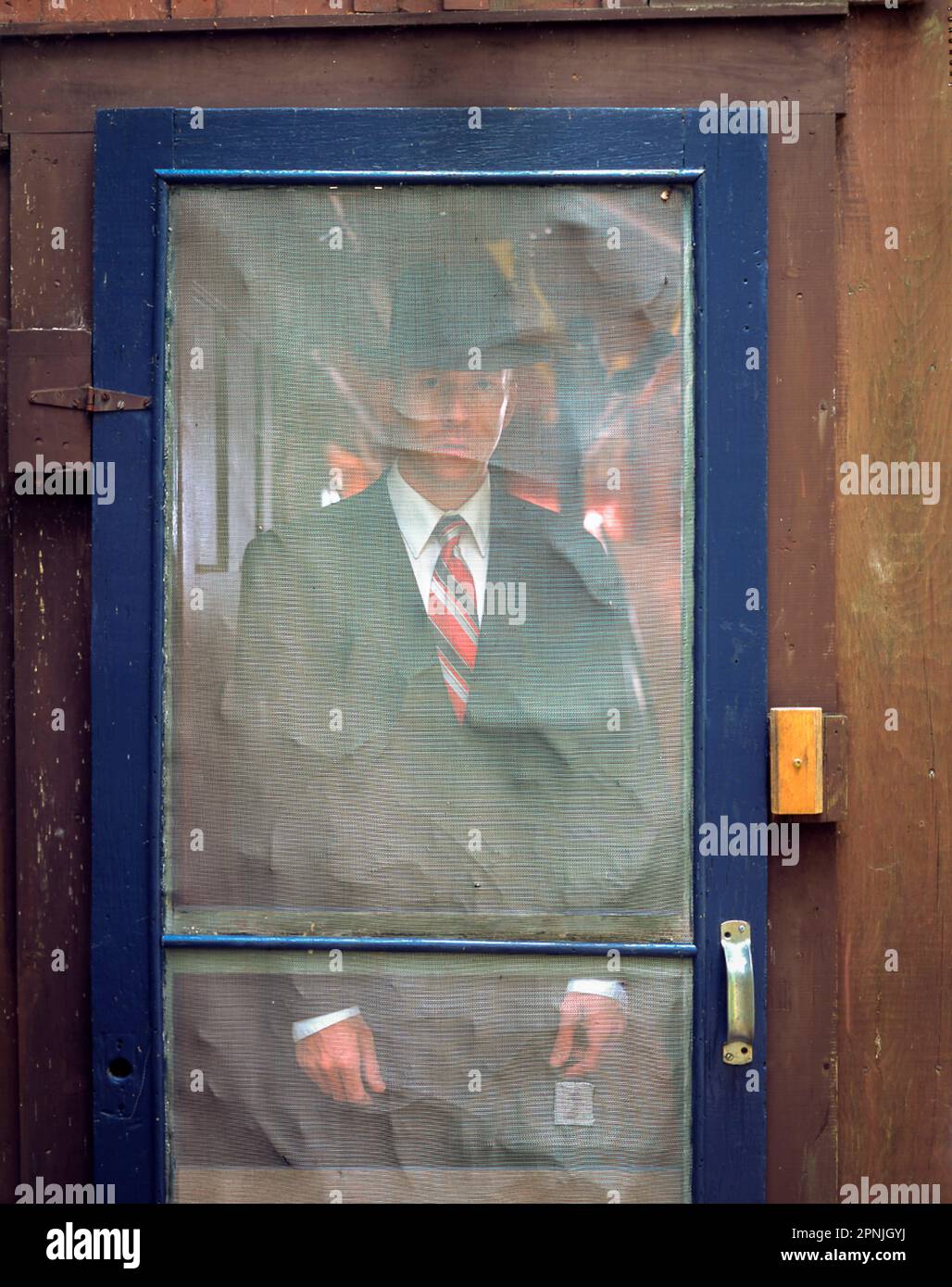 Man in suit and hat standing behind rustic screen door Stock Photo
