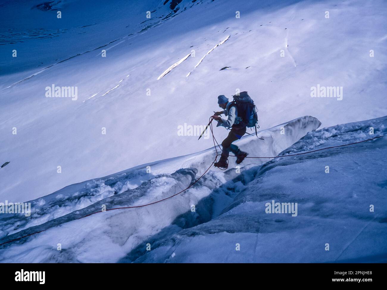 A lone climber makes a nerve wrecking jump over a crevasse on the Durand glacier on the Chamonix to Zermatt Haute Route Stock Photo