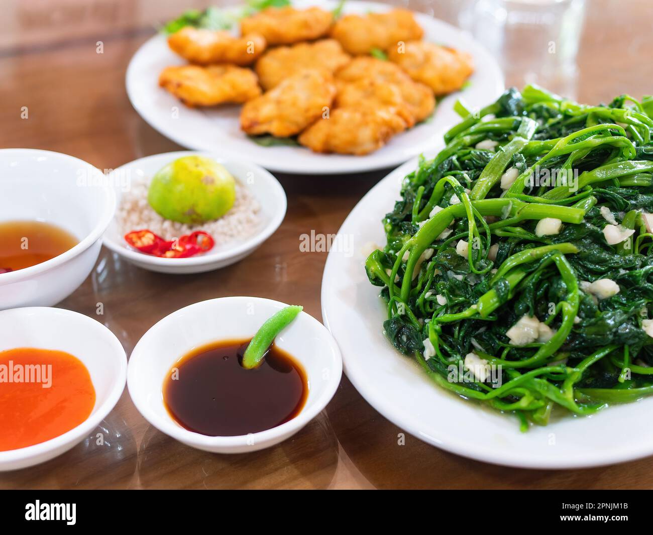Vietnamese fried morning glory, rau muong xao toi, and Vietnamese fish cakes, cha ca quy nhon, out of focus in the background. Fried morning glory is Stock Photo