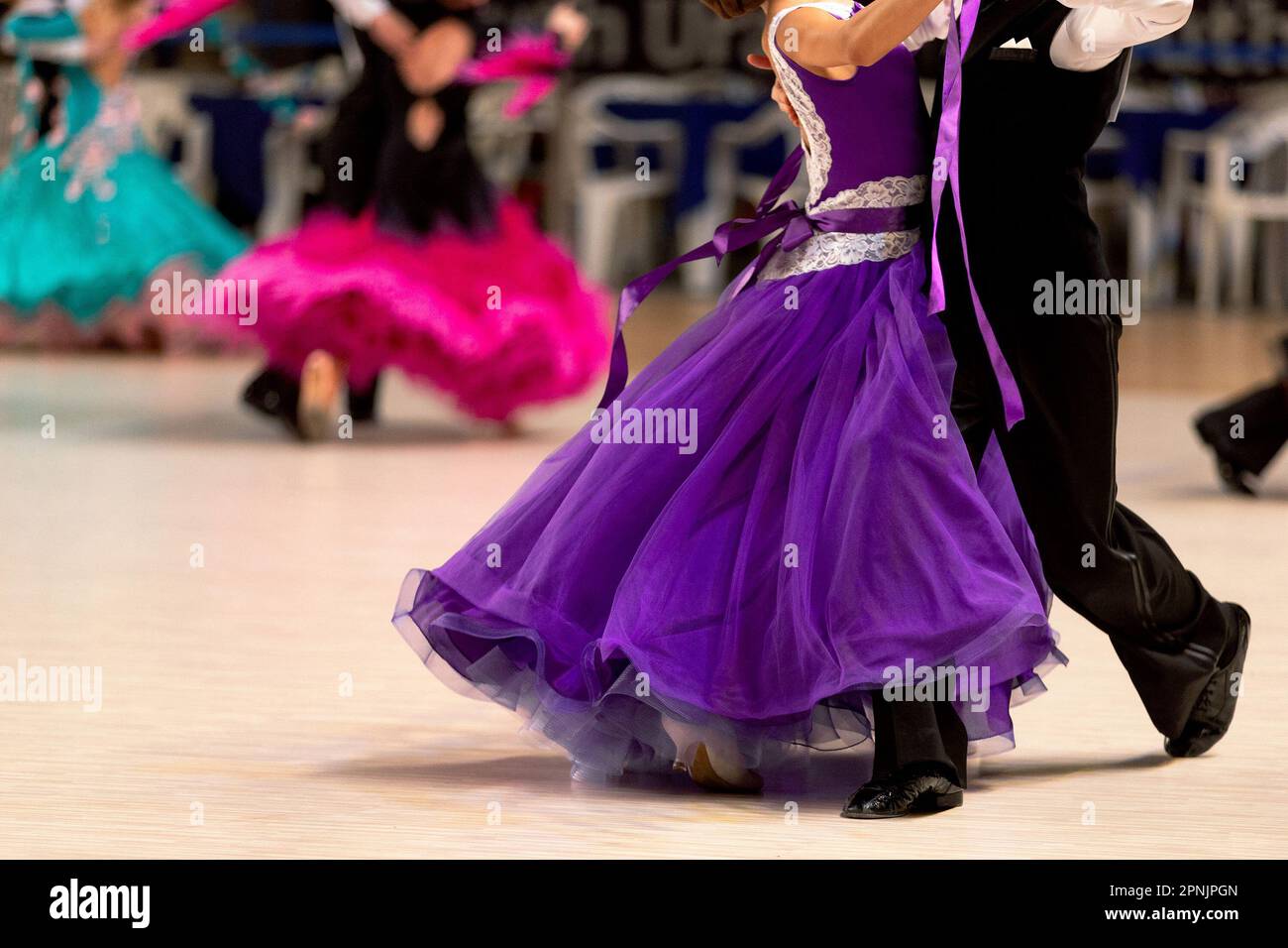 young couples dancers dancing waltz in dancesport competition, colorful dresses for girls and black tail suit for boys Stock Photo