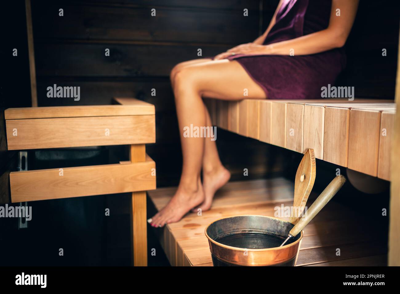 Woman in sauna in Finland. Wood steam room at summer cabin, home or hotel. Water bucket and ladle. Spa detox and healthy wellness treatment for body. Stock Photo