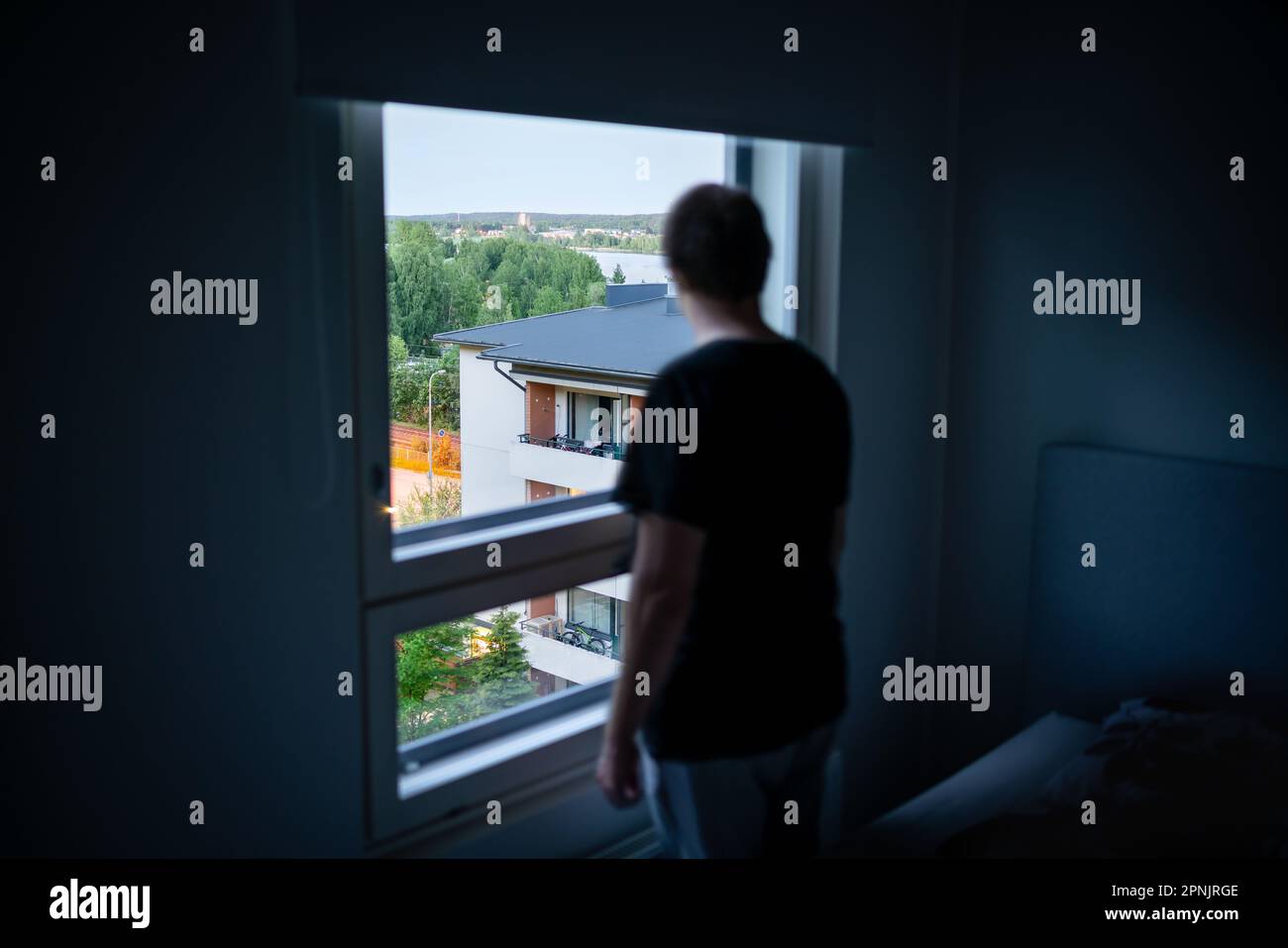 Man and window in dark room. Spying neighbor or snooping. Loneliness, shame or melancholy. Depressed, sad, moody or paranoid. Mental health. Stock Photo