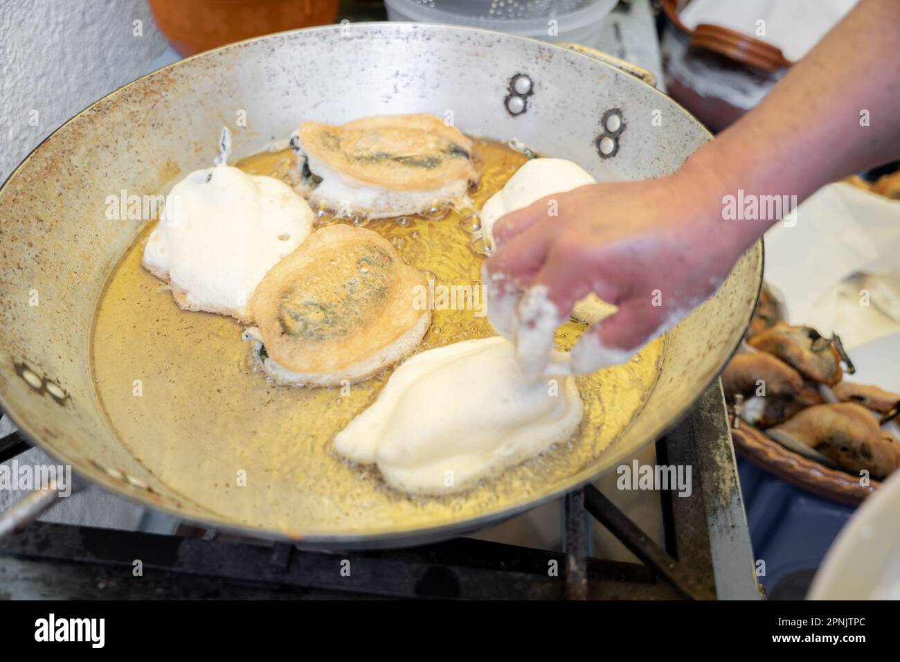 An adult Hispanic woman is frying battered poblano chilli peppers in a big metallic pan. Concept