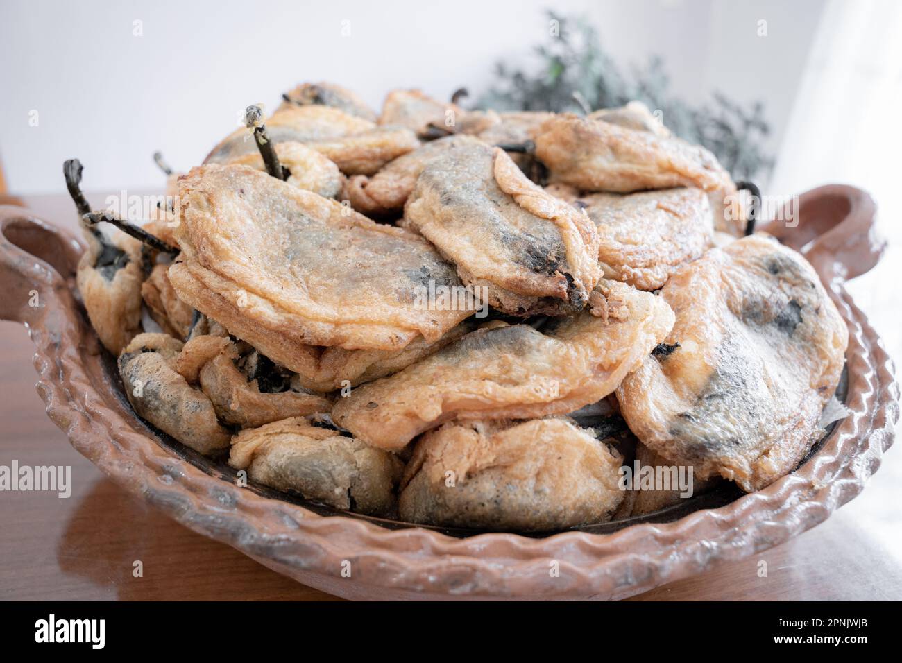 A big traditional clay casserole full of battered poblano chilli peppers resting on a table Stock Photo