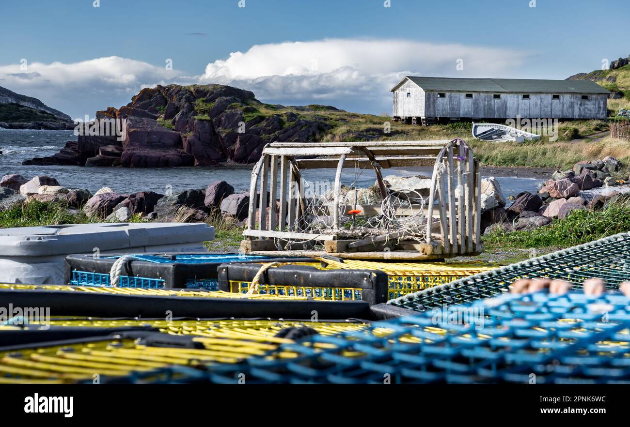 Wooden lobster trap sitting on top of other shellfish traps with a distant East Coast wooden commercial building in the Canadian maritimes at Keels Ne Stock Photo