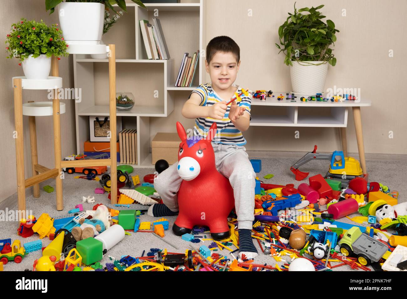 A little boy is jumping on an inflatable rubber donkey among the mess