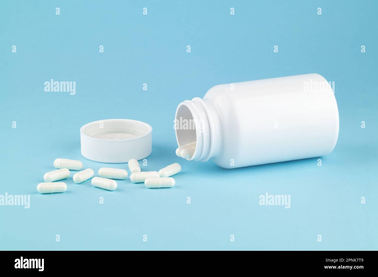 Different drugs and health supplement pills poured from a medicine white bottle health care and medical top view on colored blue background. Stock Photo