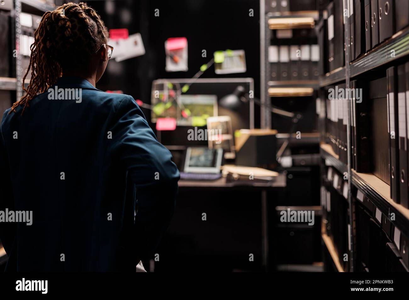 Woman police investigator standing in dark office room and looking at