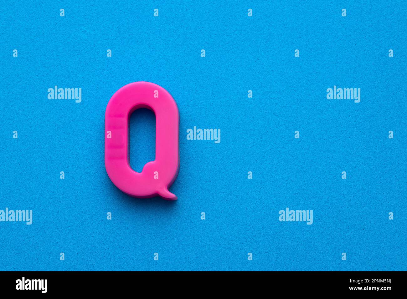 Plastic pink letter Q uppercase on blue foamy background Stock Photo