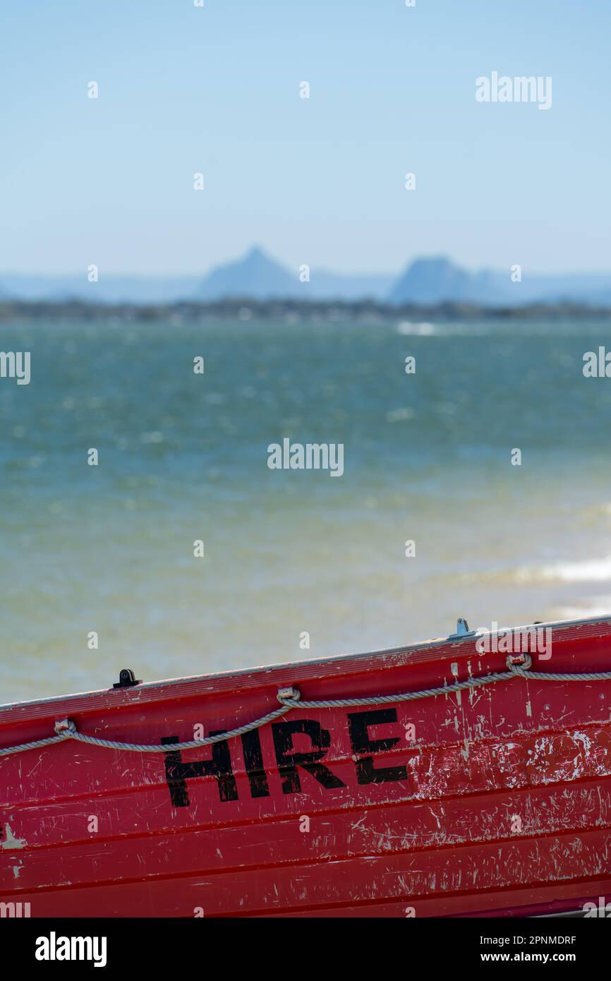 Selective focus: close up view of a red hire boat, with blurred view of sea and mountains in the background. Sylvan Beach Park,, Bribie Island, Queensland, Stock Photo
