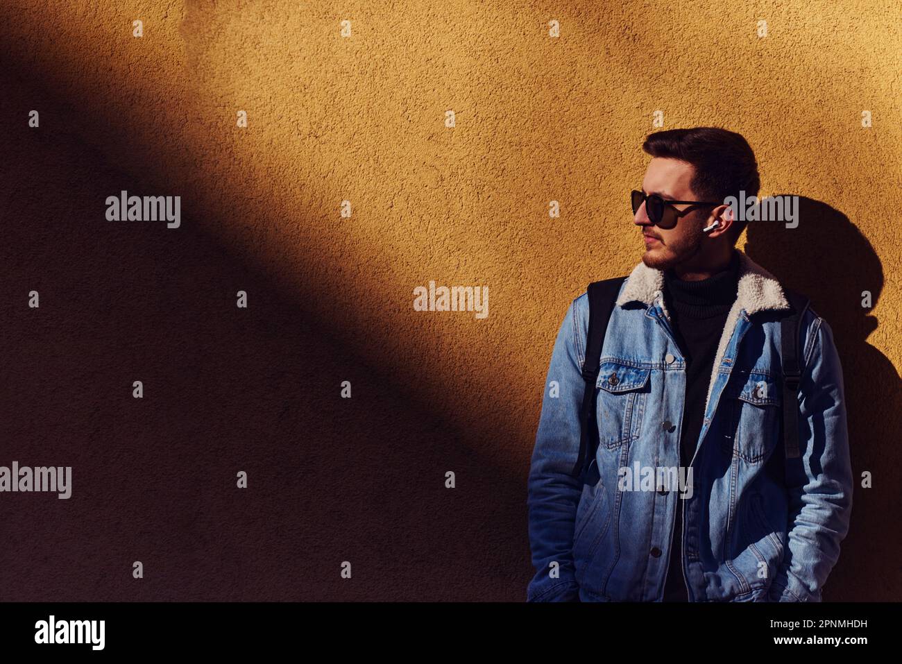 A man stands confidently in front of an orange wall, wearing sunglasses ...