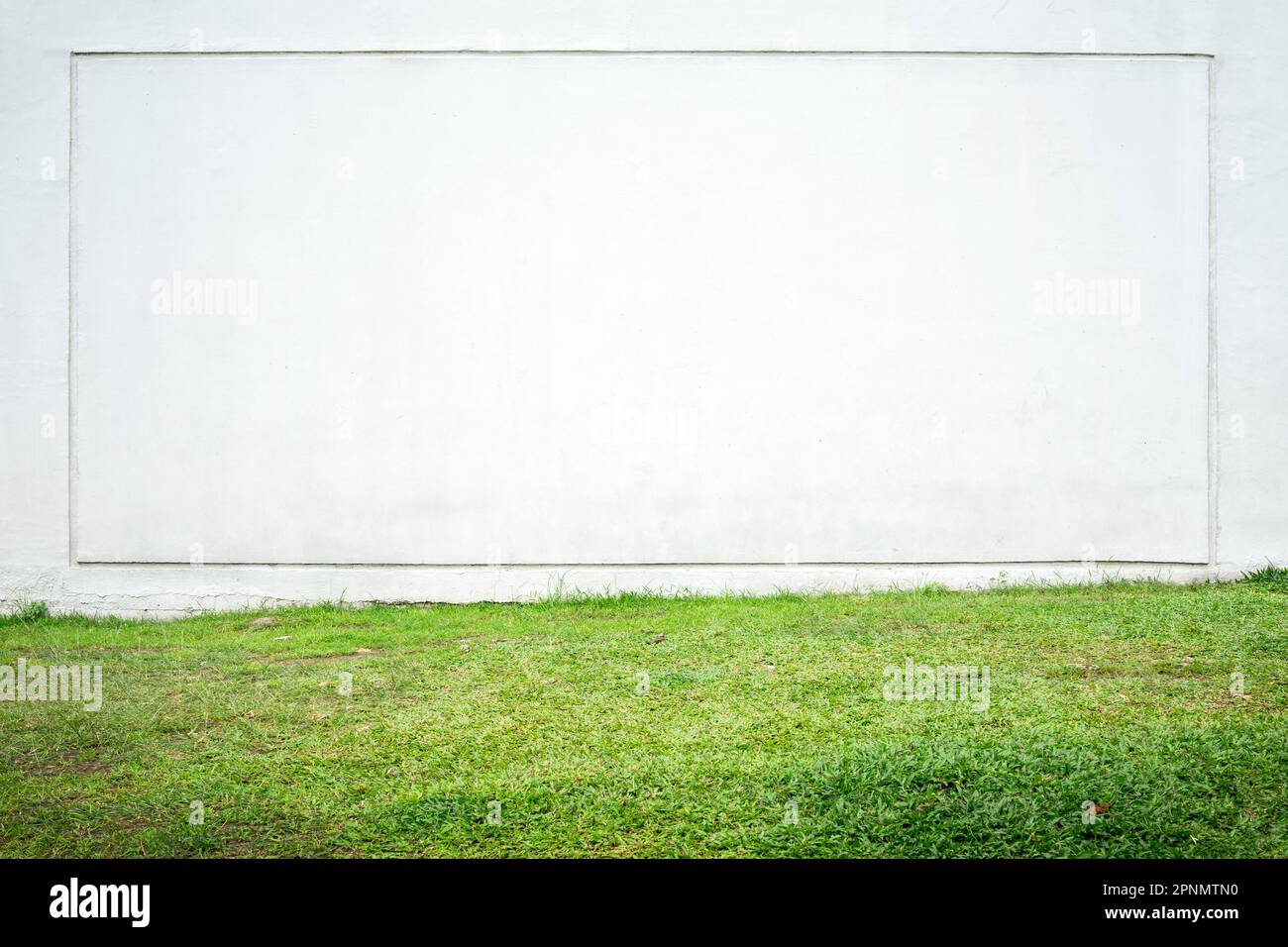 Large white wall with a square frame and green grass in the foreground
