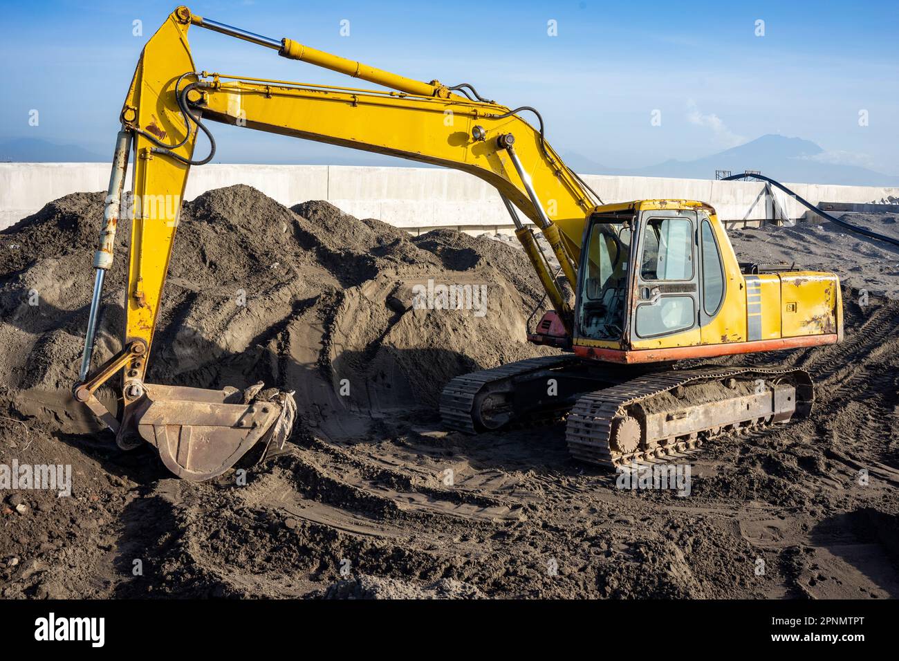 A yellow big excavator stands on a construction site with dark soil on ...
