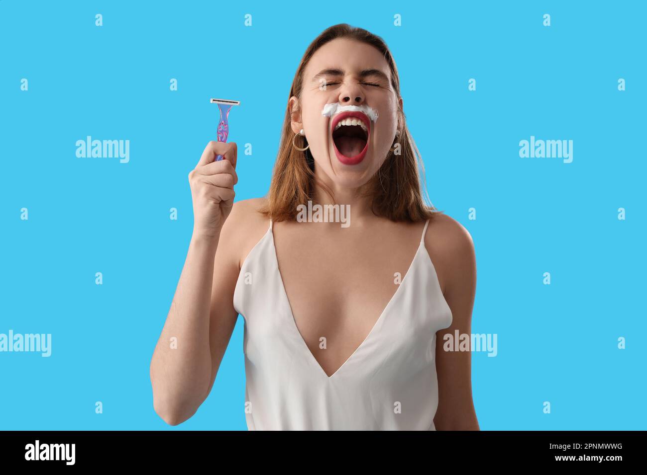 Angry young woman with shaving foam and razor on blue background Stock Photo