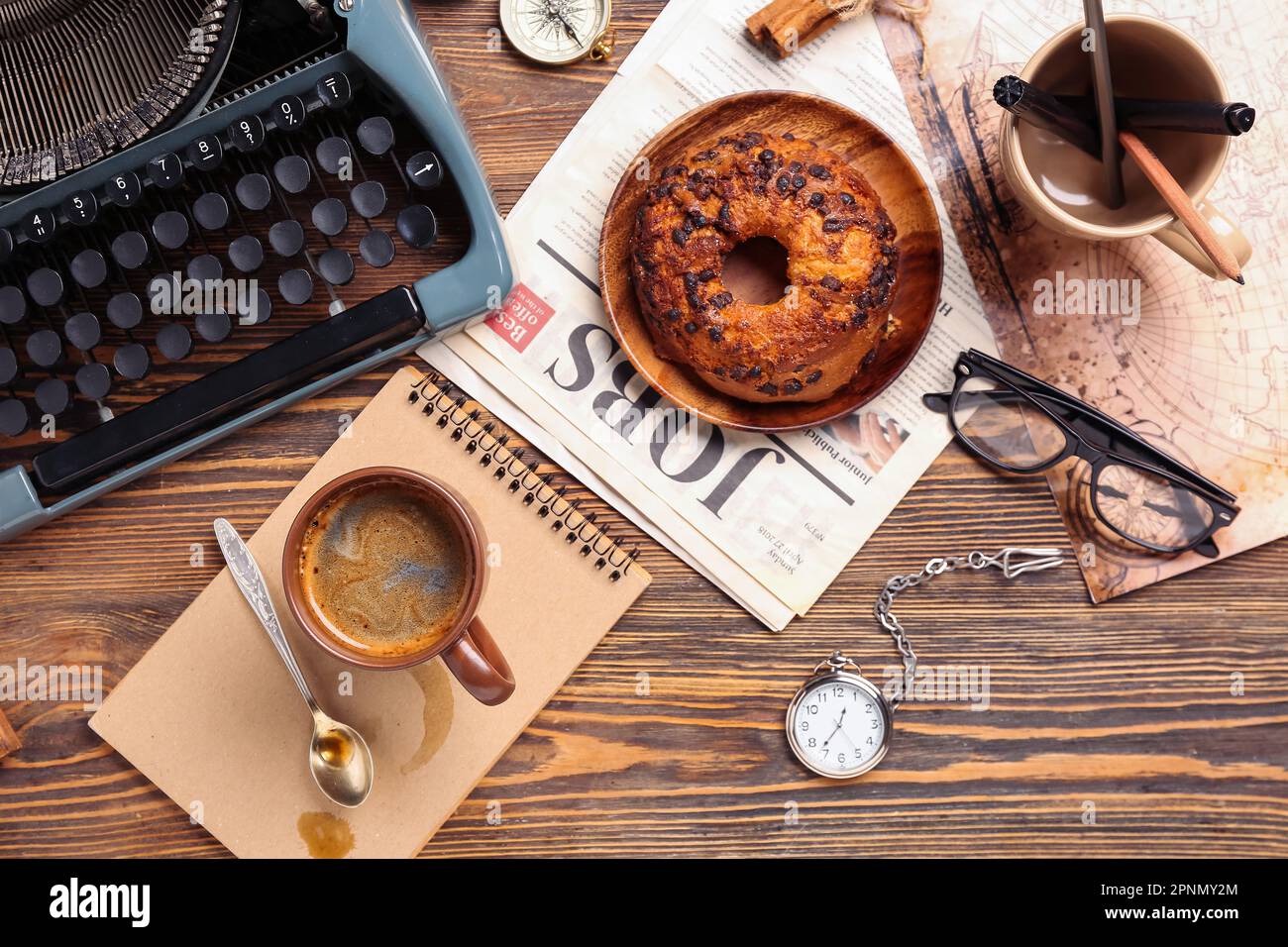 Cup of coffee with notebook, typewriter, newspaper, bun and map on wooden background Stock Photo