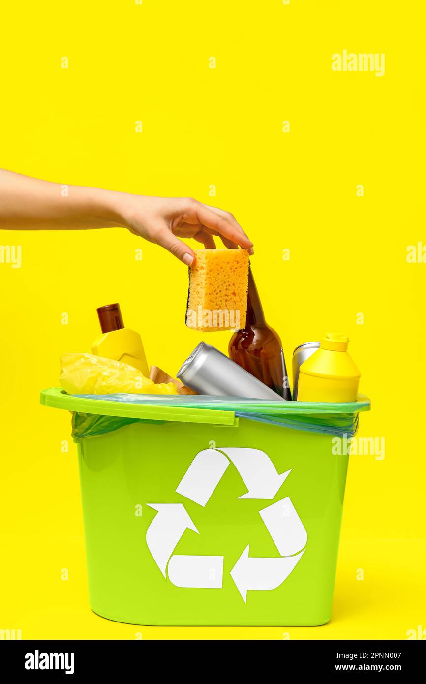 Woman throwing sponge into trash bin on yellow background Stock Photo