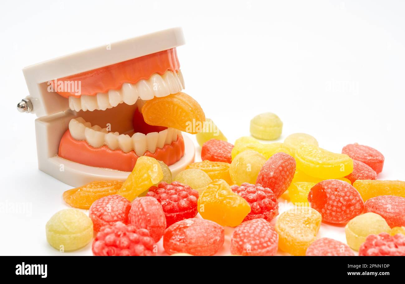 A variety of colored candies on a white background, with a tooth model biting one of the candies Stock Photo