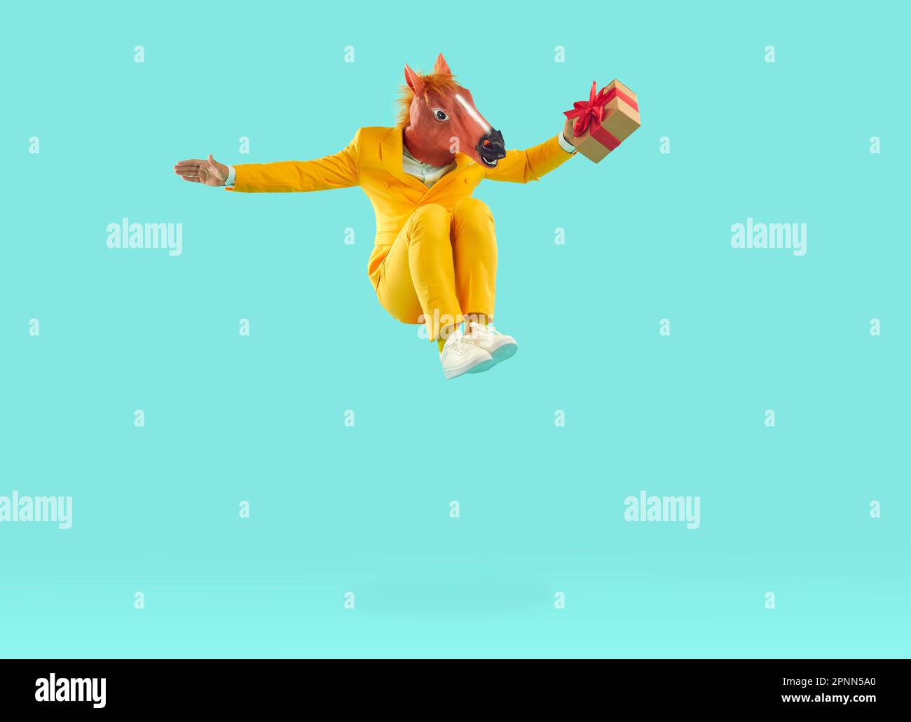 Happy man in yellow suit and funny horse mask holding gift box and