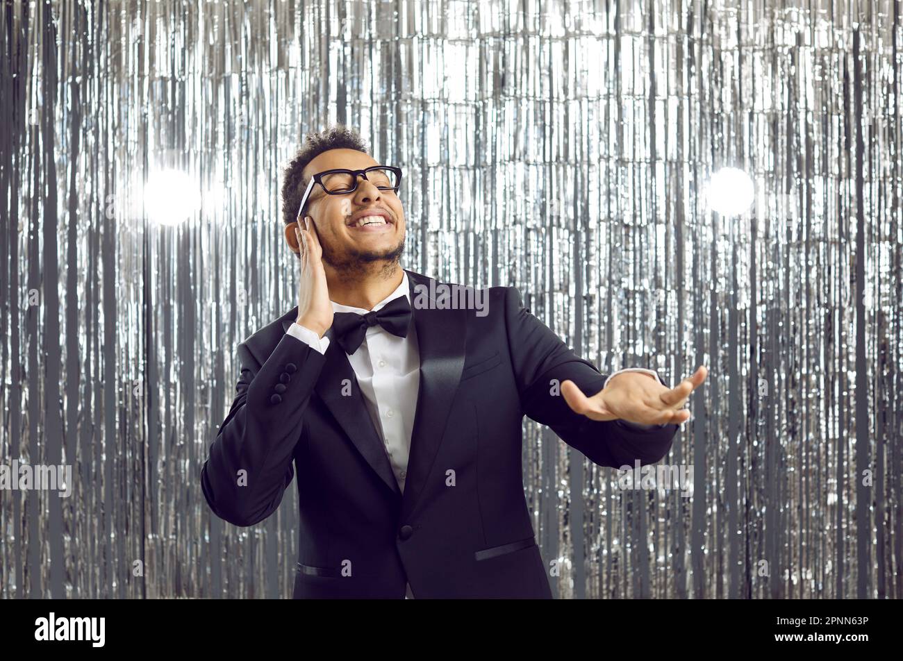 Happy funny young man in tuxedo having fun, smiling and dancing like DJ at party Stock Photo