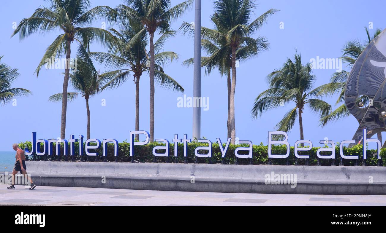 A man walks past a 'Jomtien Pattaya Beach' sign at the seaside resort of Jomtien, Pattaya, Thailand, Asia. Palm trees in background. Stock Photo