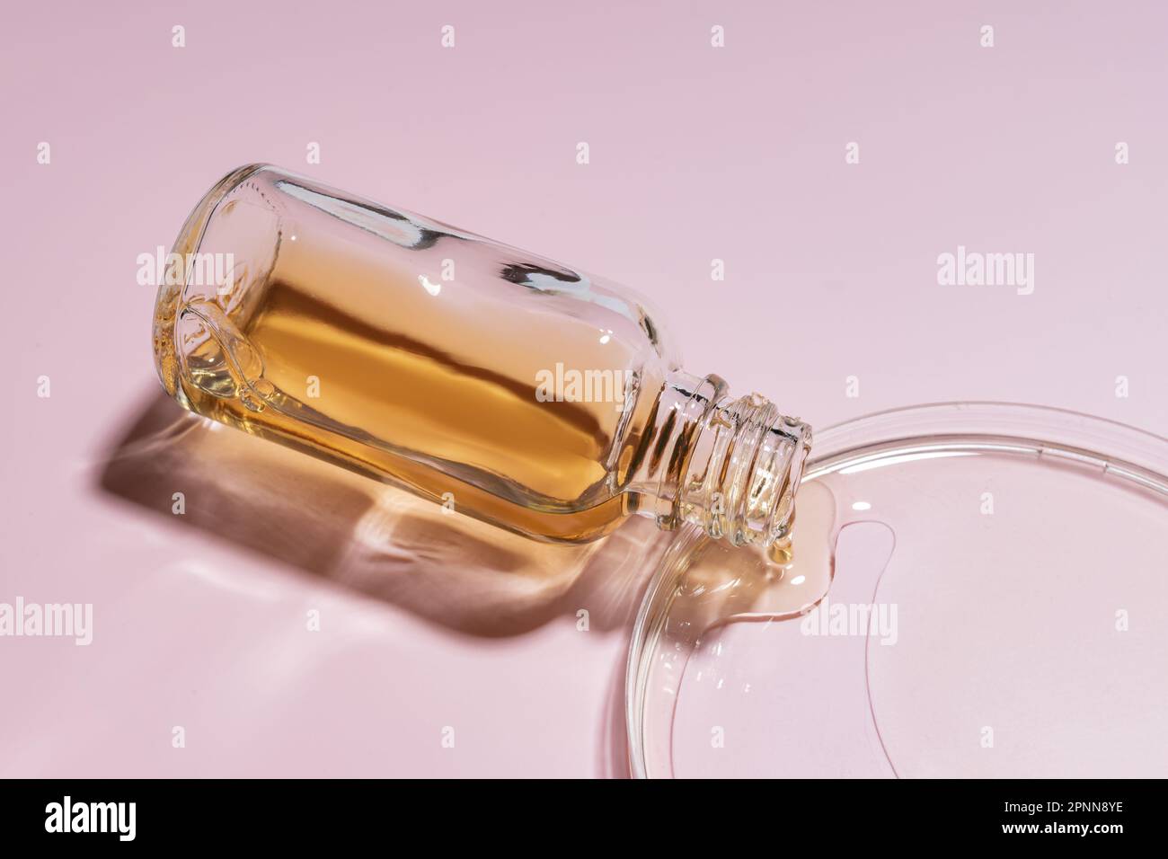 Beauty serum pours out of glass bottle into petri dish. Skin care