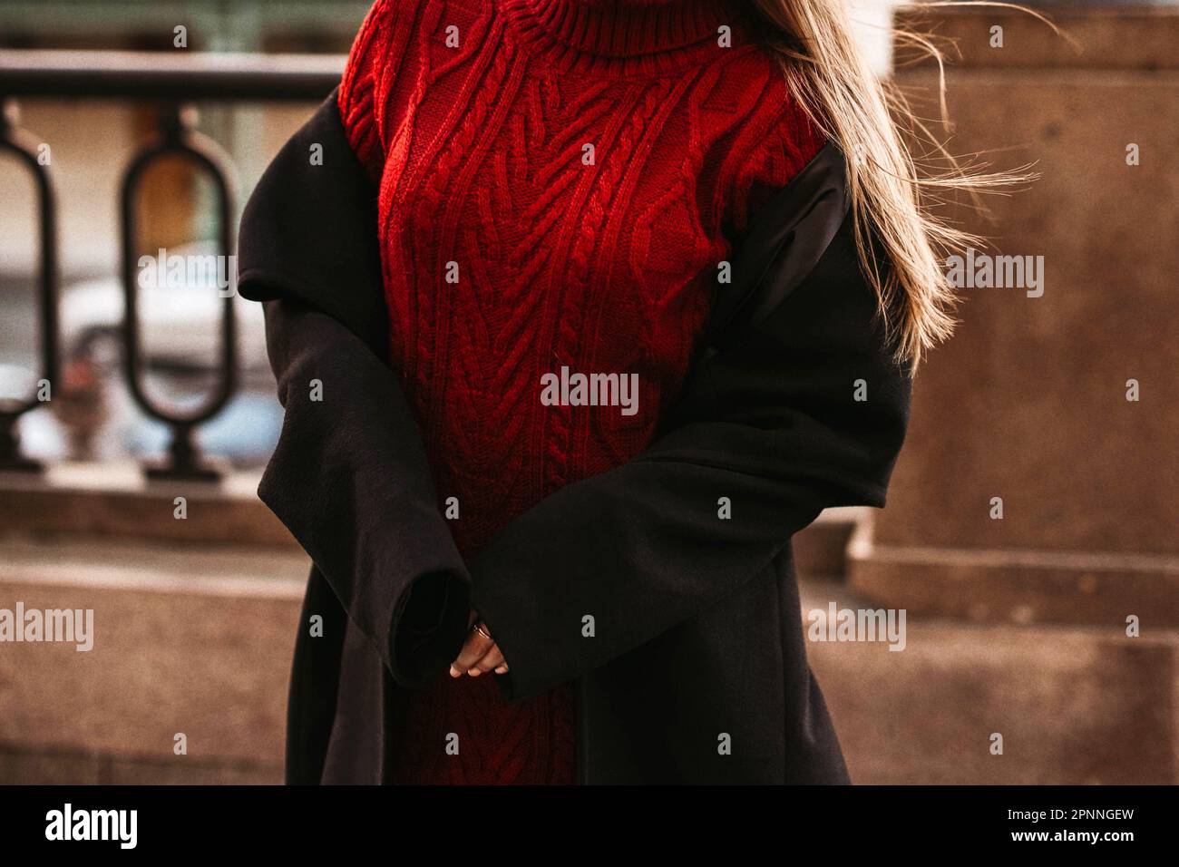 Female body in the red warm knitted sweater and black long coat. Outdoor portrait in daylight. Autumn winter street style cloth concept Stock Photo