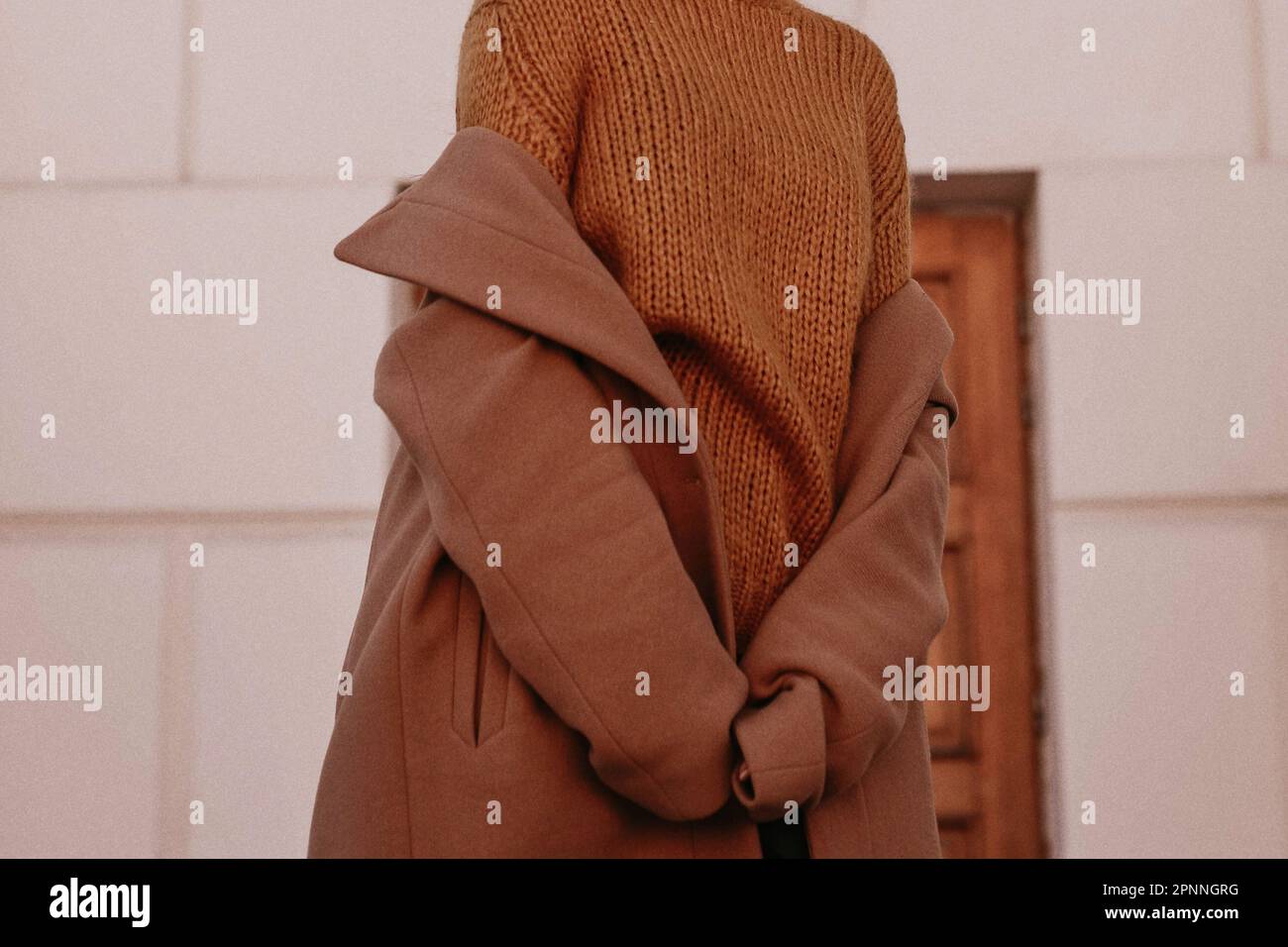 Female body in the orange warm knitting cozy sweater and long brown coat. Outdoor portrait in daylight. Autumn winter clothes street style concept Stock Photo