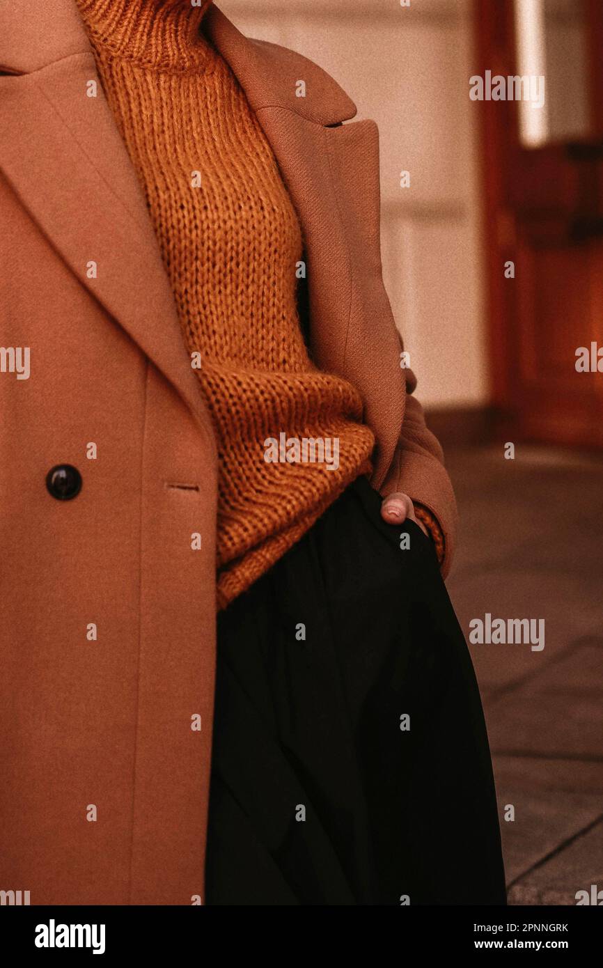 Female body in the orange warm knitting cozy sweater and long brown coat. Outdoor portrait in daylight. Autumn winter clothes street style concept Stock Photo