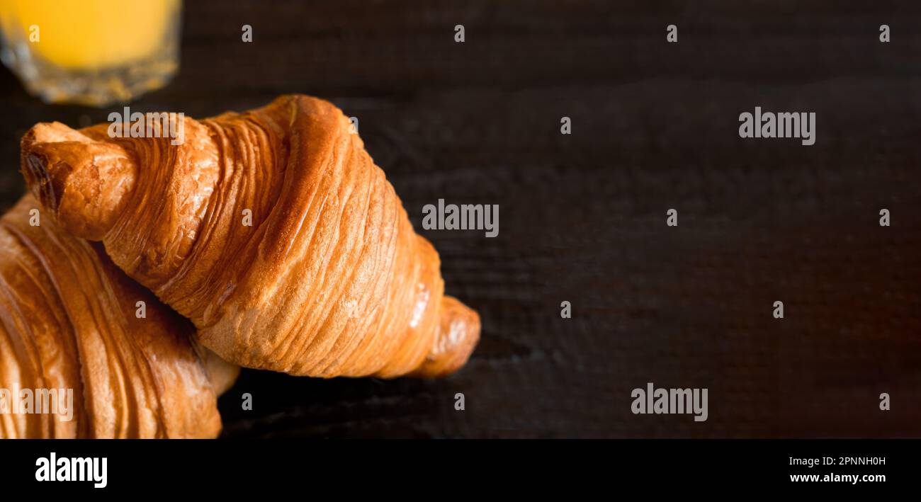 Two croissants on a wooden cutting board. Rustic dark table. Food banner. Tasty fresh croissant, jam, orange juice. Continental breakfast served with Stock Photo